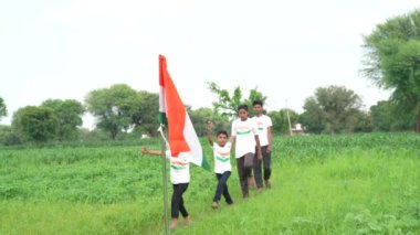 Ulusal bayrak logosu tasarımı giyen Hintli köylüler tişört basıp tutuyorlar, arka planda yeşillik olan Tricolor 'la el sallıyorlar, Bağımsızlık Günü' nü veya Cumhuriyet Günü 'nü kutluyorlar.