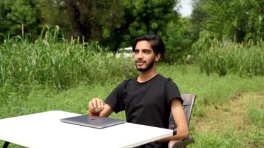 Yeşil doğa bahçesinde çalışan bilgisayar işçisi. Dışarıda dizüstü bilgisayarı olan profesyonel bir çocuk. Masada dizüstü bilgisayar kullanan genç öğrencinin tam boy kenar görüntüsü