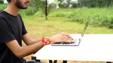 Hintli genç çocuk dizüstü bilgisayarla parkta tek başına oturuyor ve uzaktan kumandalı işleri başarıyor. Çocuk kendi dizüstü bilgisayarının projelerini kendi bitiriyor. Evden Çalışma Konsepti.