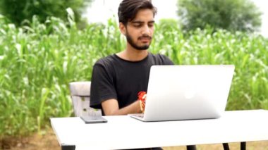 Hintli genç çocuk dizüstü bilgisayarla parkta tek başına oturuyor ve uzaktan kumandalı işleri başarıyor. Çocuk kendi dizüstü bilgisayarının projelerini kendi bitiriyor. Evden Çalışma Konsepti.