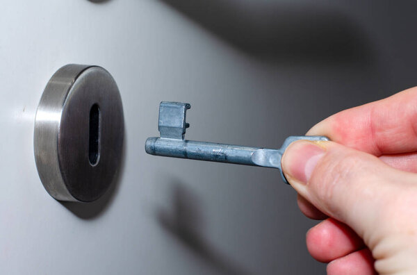 Door key in the hands of an adult man near the keyhole.
