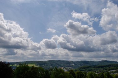 Kümülüs bulutları mavi gökyüzüne, evlere, ormanlara ve Almanya 'daki tarlalara karşı.