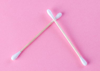 Pembe arka planda iki çapraz pamuklu çubuk, minimum konsept