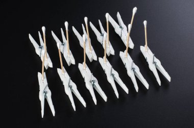 Koyu bir yüzeyde pamuklu çubuk ve mandallardan oluşan yaratıcı bir düzenleme günlük malzemelerin yaratıcı kullanımını gösteriyor.