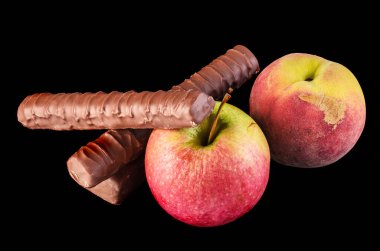 Elma, Şeftali ve Çikolata: Sağlıklı Seçim. Bir elma ve bir şeftali, siyah arka planda çikolataları cezbediyor.. 