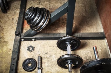 Bodrumdaki spor salonunda dambıllar ve ağırlık plakaları düzenlenmiş.