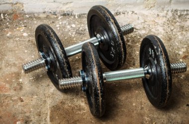 Ev jimnastik salonunun bodrumunda iki tane metal dambıl var.