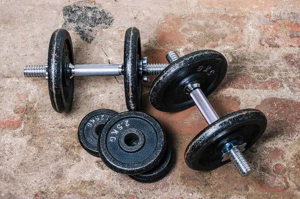 Ev bodrumunda, tuğla zeminde iki dambıl ve ağırlık plakası.