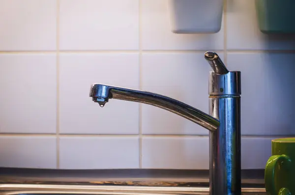 Su damlası damlayan eski krom mutfak musluğu beyaz seramik seramik seramik duvarlı arka planda su atığı ve su atığı konseptini gösteriyor..