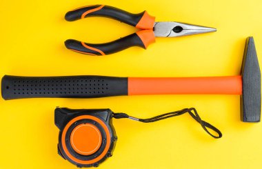 Sarı arkaplan inşaat araçları üzerinde çekiç mezurası ve pense üst görünümü