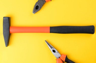 Her iki tarafta kırpılmış pense ve parlak sarı arka plan görüntüsüyle ortadaki çekiç.