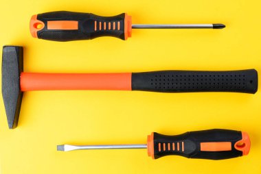 Parlak sarı zemin üzerinde çift tornavida ve çekiç, üst görünüm araçları