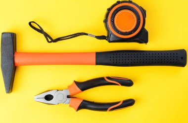 Sarı arkaplanda pense, çekiç ve mezura, üst görünüm araçları ayarlandı