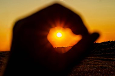 Güneş, el siluetiyle çerçeveleniyor. Turuncu gökyüzü arka planına karşı 