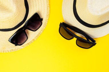 Sarı arka planda iki güneş gözlüklü iki hafif plaj şapkası.