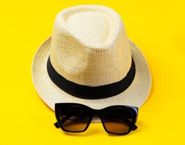 Sarı arka planda duran güneş gözlüklü şapka yaz moda konsepti.