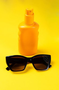 Sarı arka planda güneş kremi ve güneş gözlüğü yaz tatili konsepti