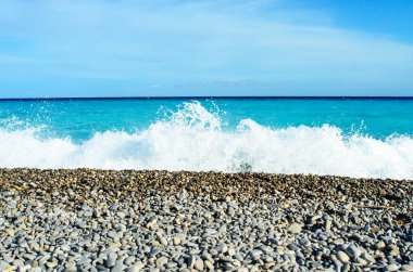 Dalgalar, turkuaz su ve güzel Fransa 'da parlak gökyüzü ile çakıl taşı kıyılarına yuvarlanıyor.