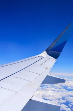 Sonsuz mavi gökyüzüne ve kabarık beyaz bulutlara karşı uçak kanatları