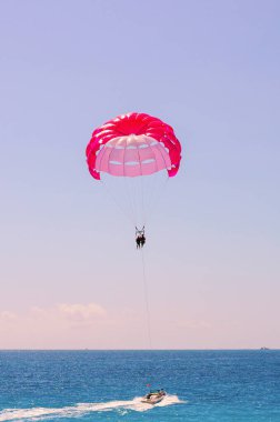Motorlu tekne, parlak mavi gökyüzünün altında sakin denizin üzerinde iki paraşütçüyü çekiyor.