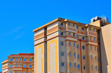 Terasotta çatıları, balkonları ve açık gökyüzünün altında mavi pencereleri olan alçılı binalar..