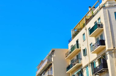 Yeşil bitkiler ve mimari detaylarla dolu balkonların bulunduğu modern konut binalarının üzerinde mükemmel mavi gökyüzü.