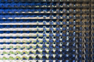 Dikey oyuklar ve ışık yansımaları arka planına sahip desenli kaburgalı cam yüzeyin yakınlaştırılması