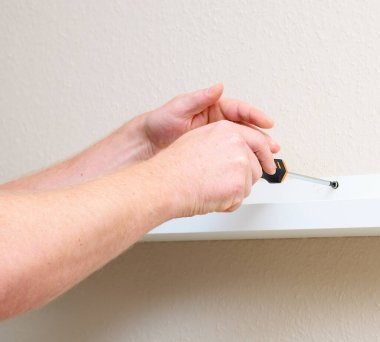 Beyaz rafı tornavidayla duvara vidalayan adam, yakın plan el ve iş.