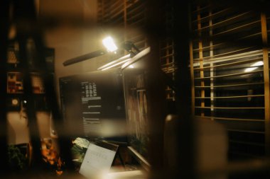 Pencere perdelerinden sinema masasına sessiz ve samimi bir bakış. Yumuşak, ılık ışıklar ve bulanık çizgiler nostaljik ve yansıtıcı bir atmosferi çağrıştırıyor..