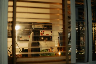 Pencere perdelerinden sinema masasına sessiz ve samimi bir bakış. Yumuşak, ılık ışıklar ve bulanık çizgiler nostaljik ve yansıtıcı bir atmosferi çağrıştırıyor..