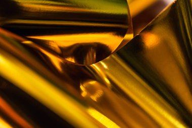 Dinamik kıvrımları ve yansımaları olan parlak altın folyonun yüksek çözünürlüklü yakın çekimi. Lüks markalaşma, paketleme veya dijital tasarım projelerinde kullanmak için zarif metalik dokuyu yakalar.