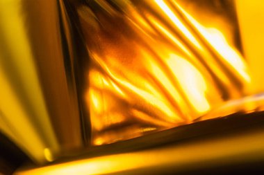 Dinamik kıvrımları ve yansımaları olan parlak altın folyonun yüksek çözünürlüklü yakın çekimi. Lüks markalaşma, paketleme veya dijital tasarım projelerinde kullanmak için zarif metalik dokuyu yakalar.