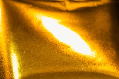 Dinamik kıvrımları ve yansımaları olan parlak altın folyonun yüksek çözünürlüklü yakın çekimi. Lüks markalaşma, paketleme veya dijital tasarım projelerinde kullanmak için zarif metalik dokuyu yakalar.