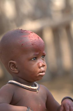 Küçük oğlan bir sandalyede oturuyor. Çocuk kafasına bakıyor.