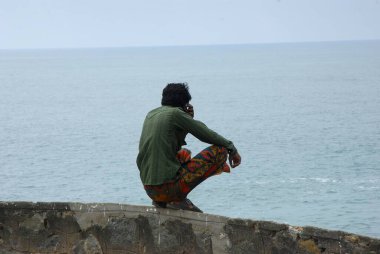 Genç adam sahilde oturuyor.