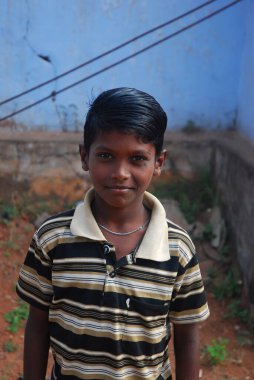 Kafası arka planda kameraya bakan genç bir çocuğun portresi.