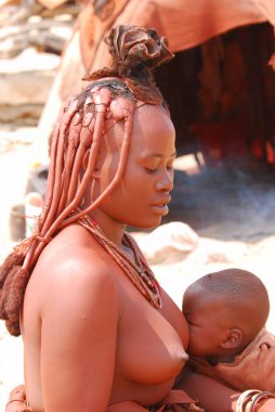 Genç bir kadın çıplak Afrikalı kadınının kumunda oturuyor.