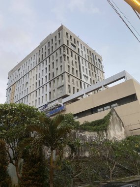 Mavi gökyüzü geçmişi olan yeşil ağaçların arasında bir otel binası..