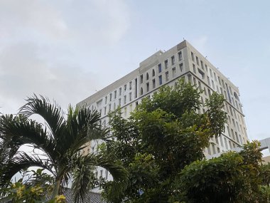 Mavi gökyüzü geçmişi olan yeşil ağaçların arasında bir otel binası..