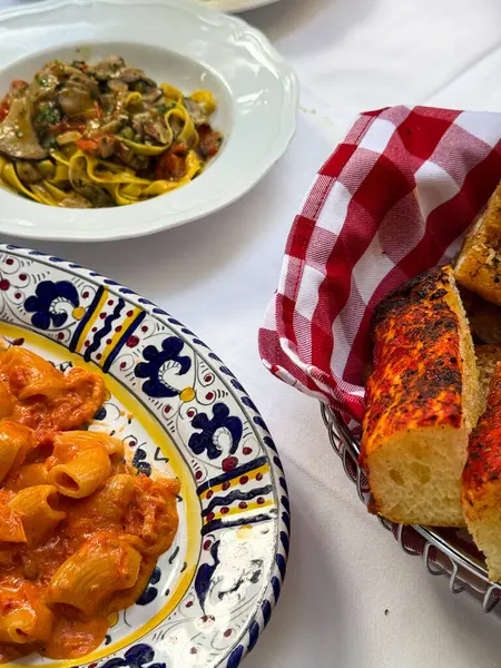 İtalyan yemeği, rigatoni, Focaccia ve spagetti, desenli tabaklar ve kırmızı kareli peçeteyle süslenmiş..