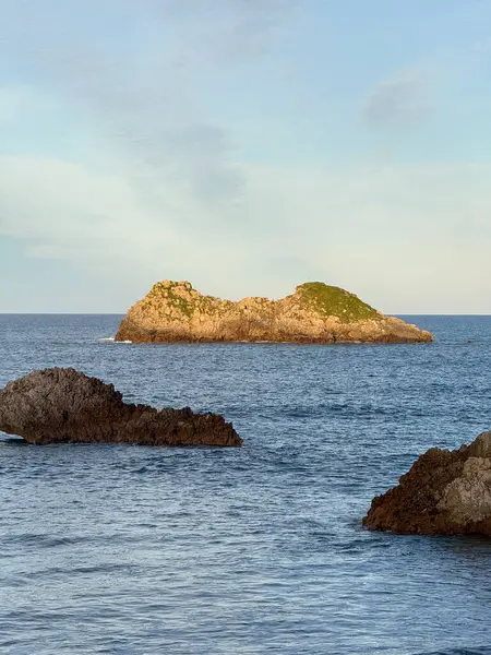 Okyanustan üç kayalık ada yükseliyor, biri sakin bir sahil sahnesinde berrak bir gökyüzünün altında altın saat ışığıyla parıldıyor..
