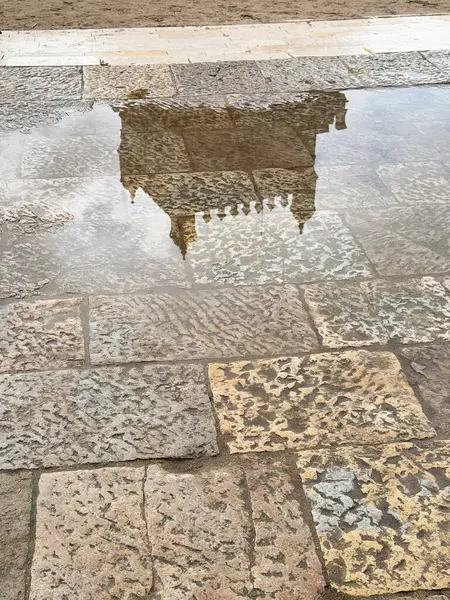 Lizbon 'da bir kaldırımda su birikintisindeki tarihi bir kulenin yansıması, eski mimariyi kentsel detaylarla birleştirmek..