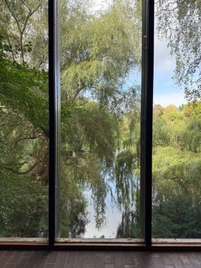 Scenic view of green trees and a lake framed by a full-length window in Copenhagen, Denmark.