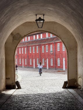 Woman cycling across the background of a historic stone tunnel with cobblestone floor in Copenhagen.