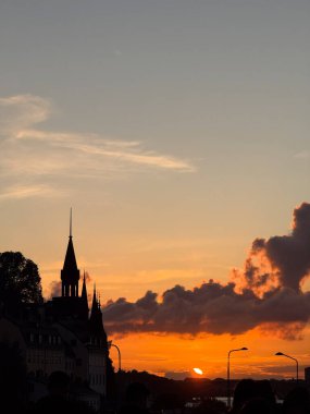 High contrast Stockholm skyline silhouette with orange sunset and clouds in the back.