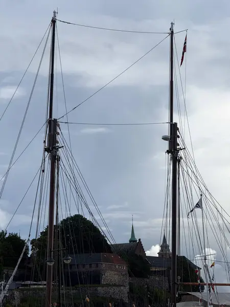 A view of tall wooden masts of a docked boat against a cloudy sky in Oslo marina.
