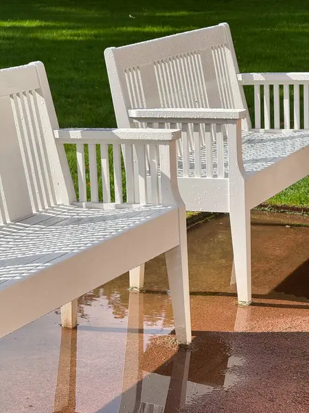 Two white benches placed on a wet sidewalk in Oslo after rainfall.