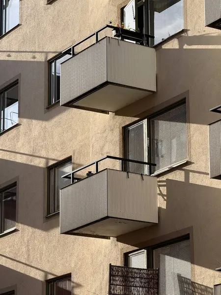Square balconies on yellow building casting strong angular shadows in Stockholm.