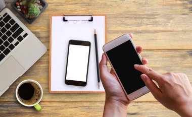 Akıllı telefon ve dizüstü bilgisayar, akıllı telefon, Pano, çiçek, kalem ve kahve ofis Resepsiyon arka planda tutan el. İş amaçlı aksesuarları tablo ile çalışma alanı için ev ofis.