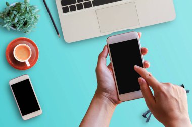 Akıllı telefon ve dizüstü bilgisayar, akıllı telefon, gözlük, çiçek, kalem ve kahve ofis Resepsiyon arka planda tutan el. İş amaçlı aksesuarları tablo ile çalışma alanı için ev ofis.